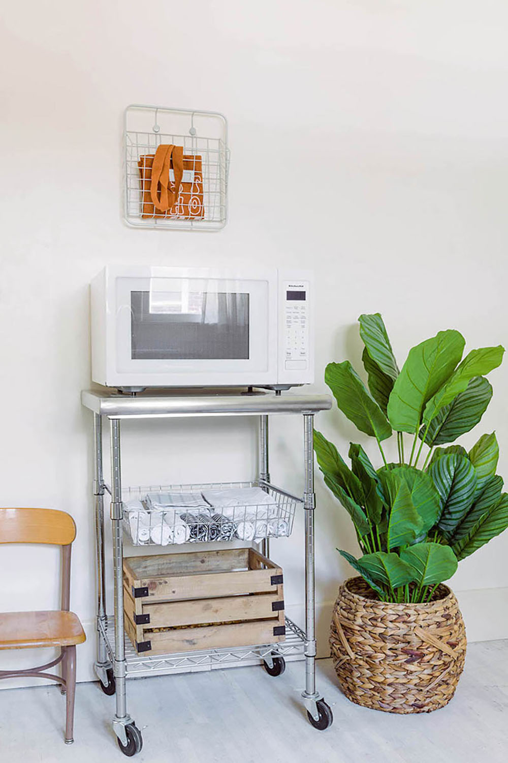 Microwave sitting on top of kitchen cart with baskets and decor