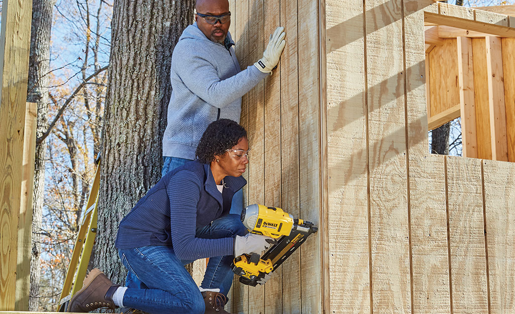 Couple attaches siding to a treehouse frame.