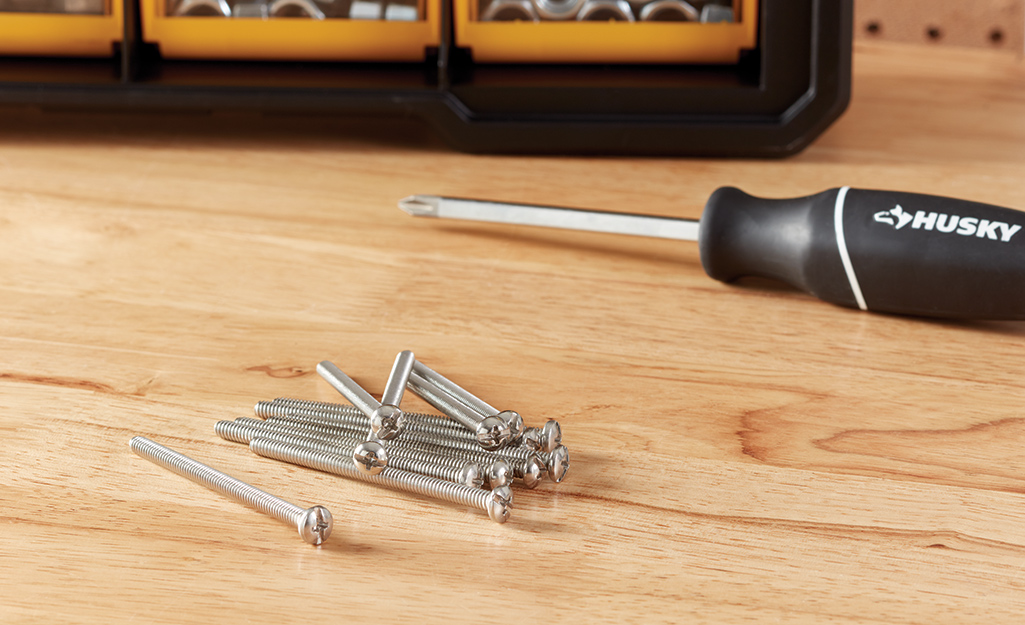 Machine screws lay next to a screwdriver on a wood surface.