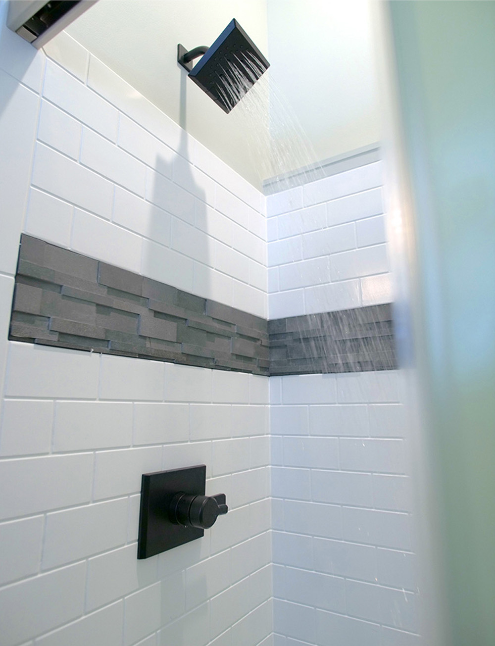 Shower with black shower head and white and grey tile.