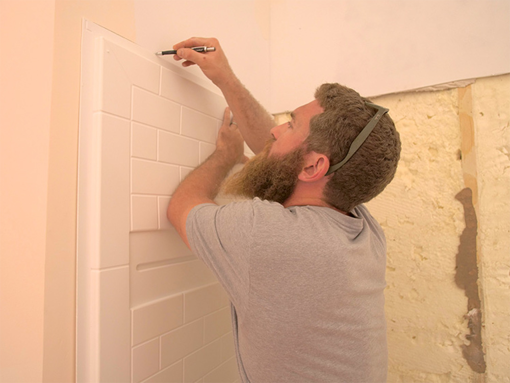 Man measuring a wall and white shower tile. 
