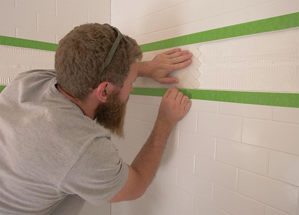 Man installing white bathroom tile.