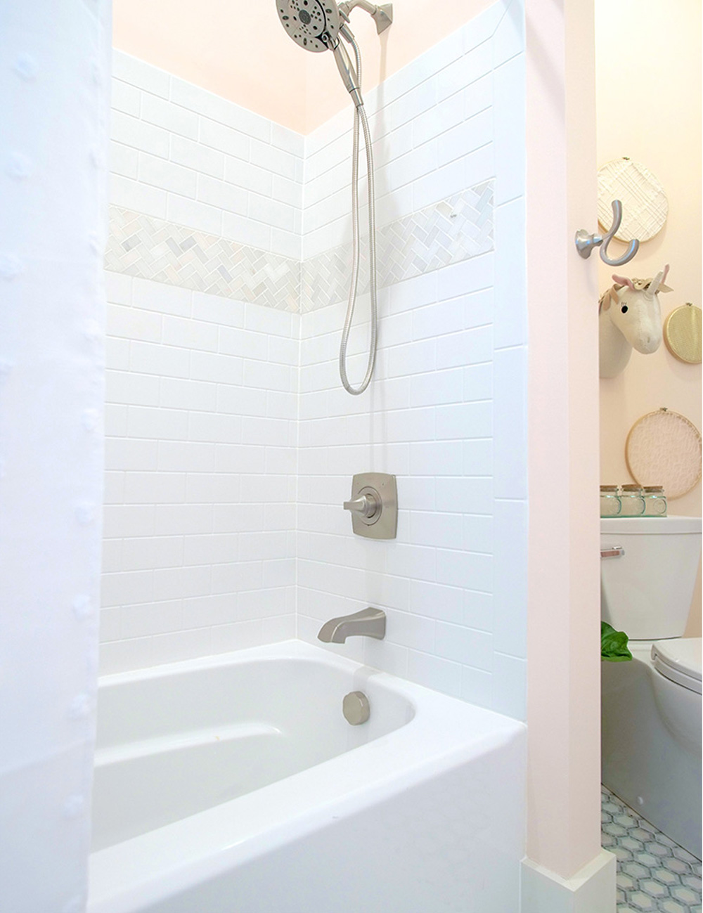 Shower area with a white tub, white and grey tile, silver shower head and faucet, and a white shower curtain.