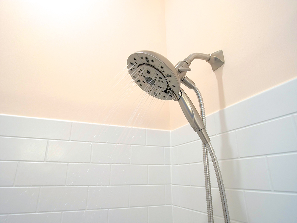 Silver shower head, white tile and peach painted wall.