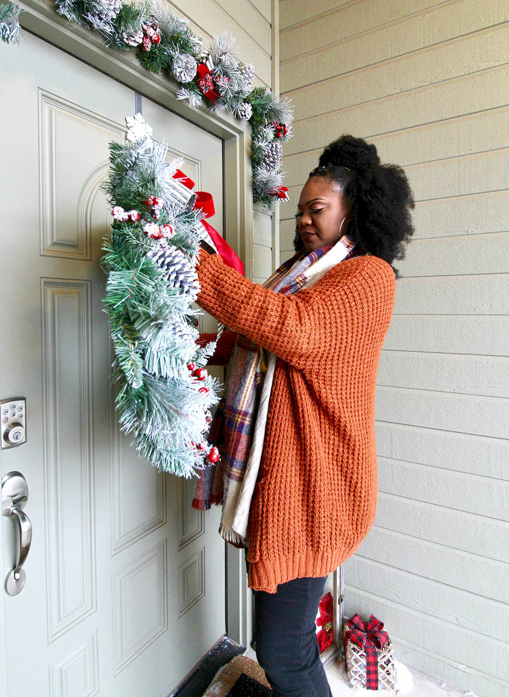 A woman hanging a Christmas wreath on a front door.