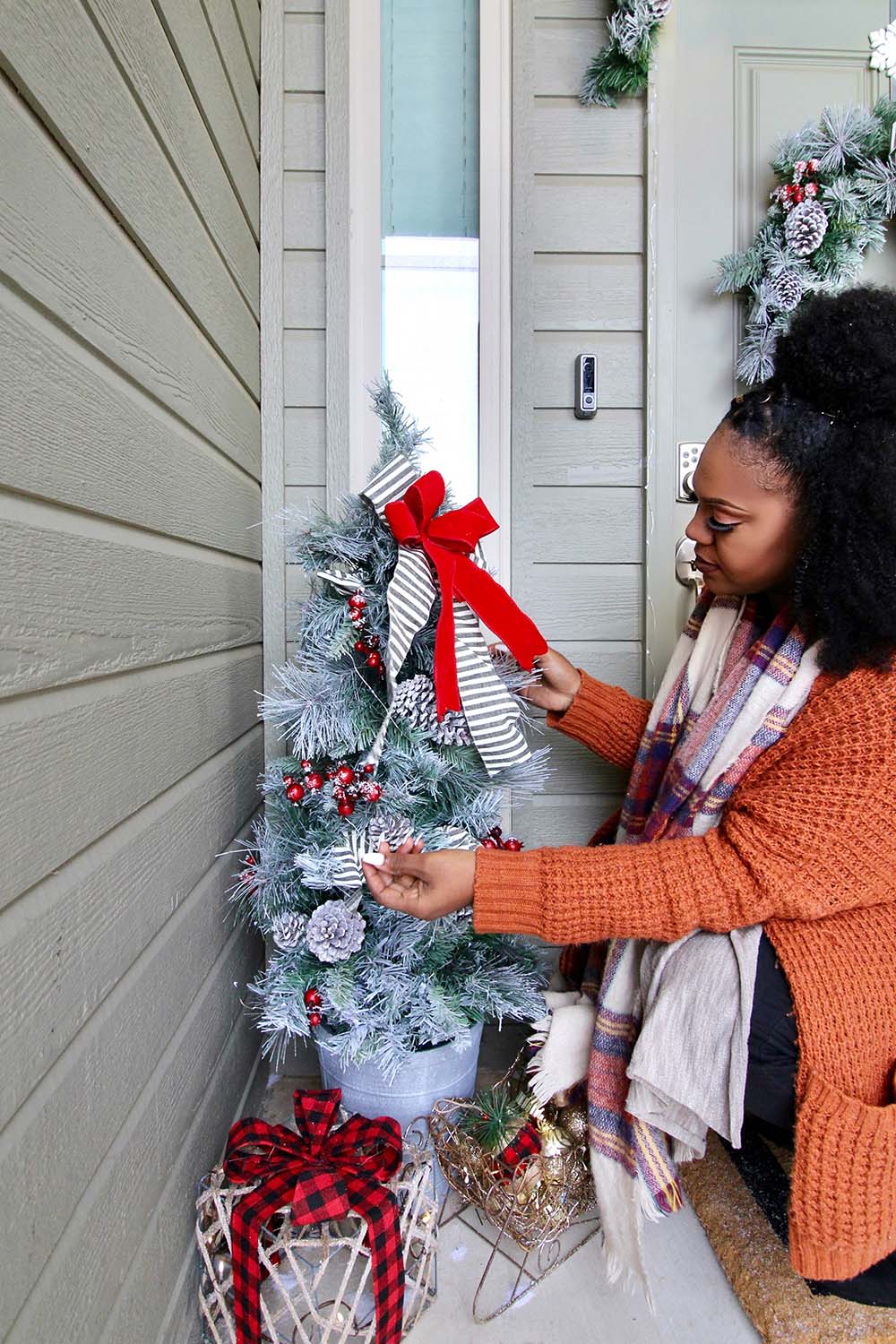A woman touches a porch Christmas tree decorate with snowy pinecones and berries.
