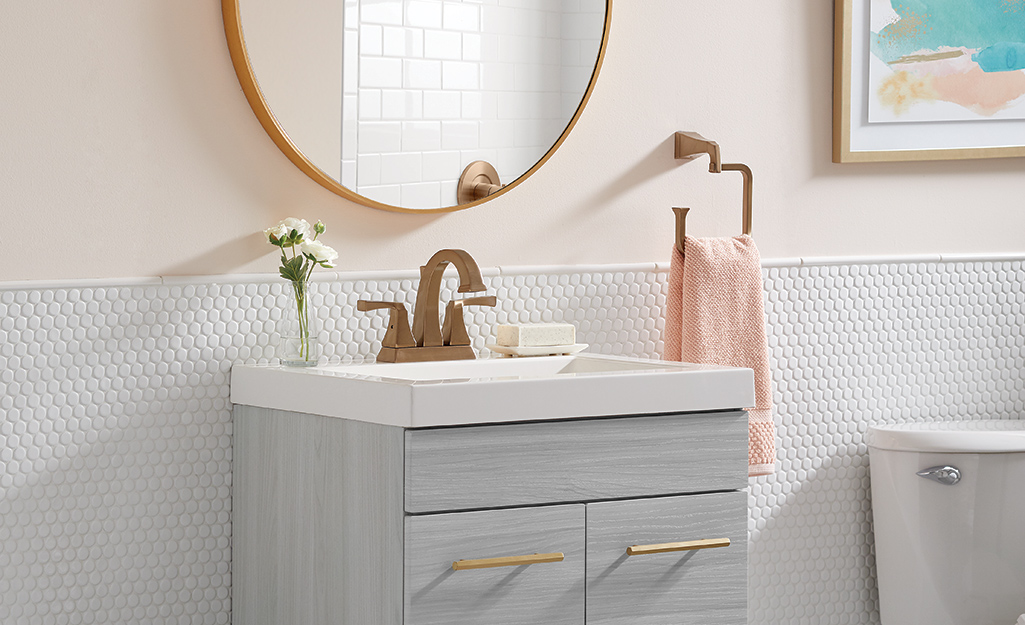 A bathroom vanity accented by a gold faucet, mirror and towel holder.