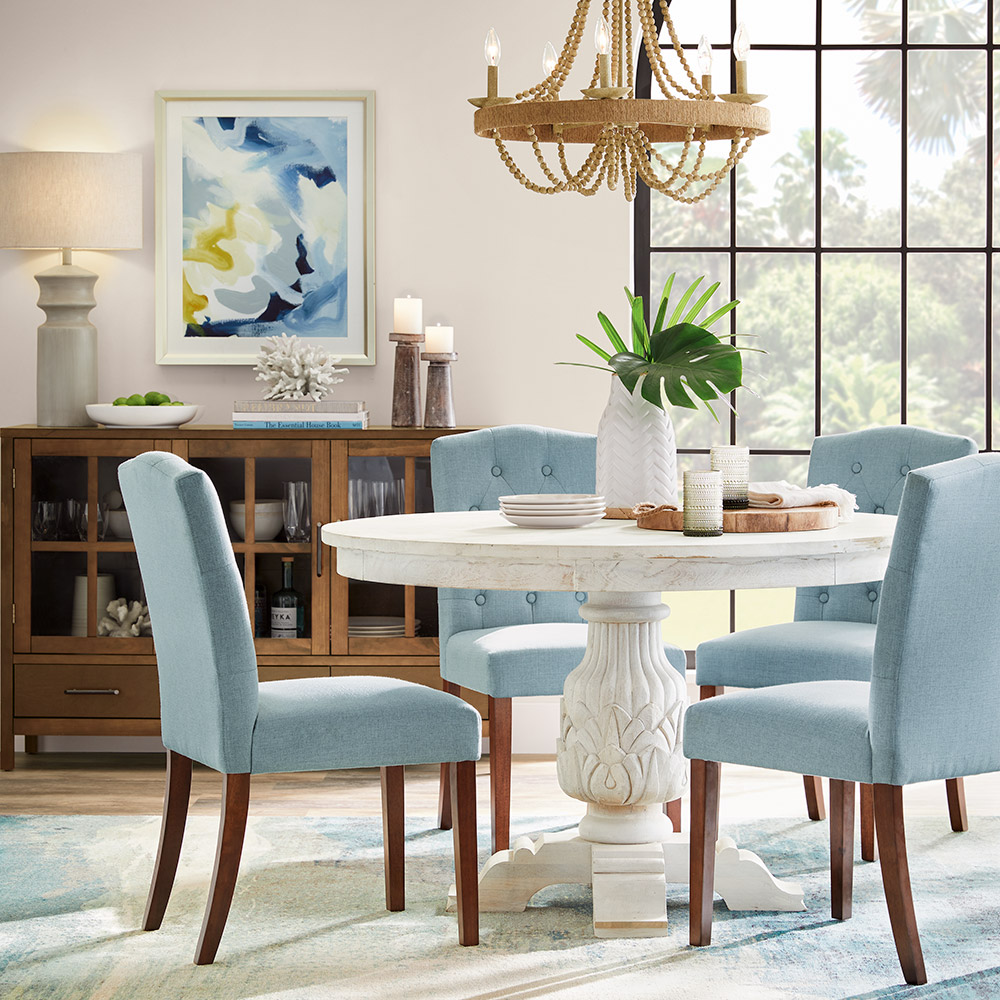 Four light blue upholstered chairs sit around a round dining room table.