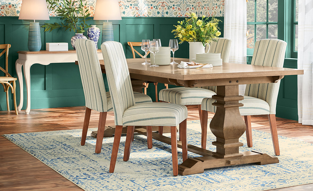 Four chairs with white upholstery stand around a rectangular dining room table.