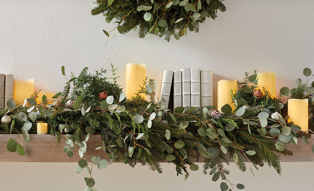 A fireplace mantel decked with fresh greenery and candles.