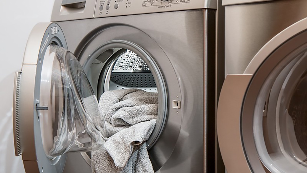 A silver front-load dryer open with towels inside.