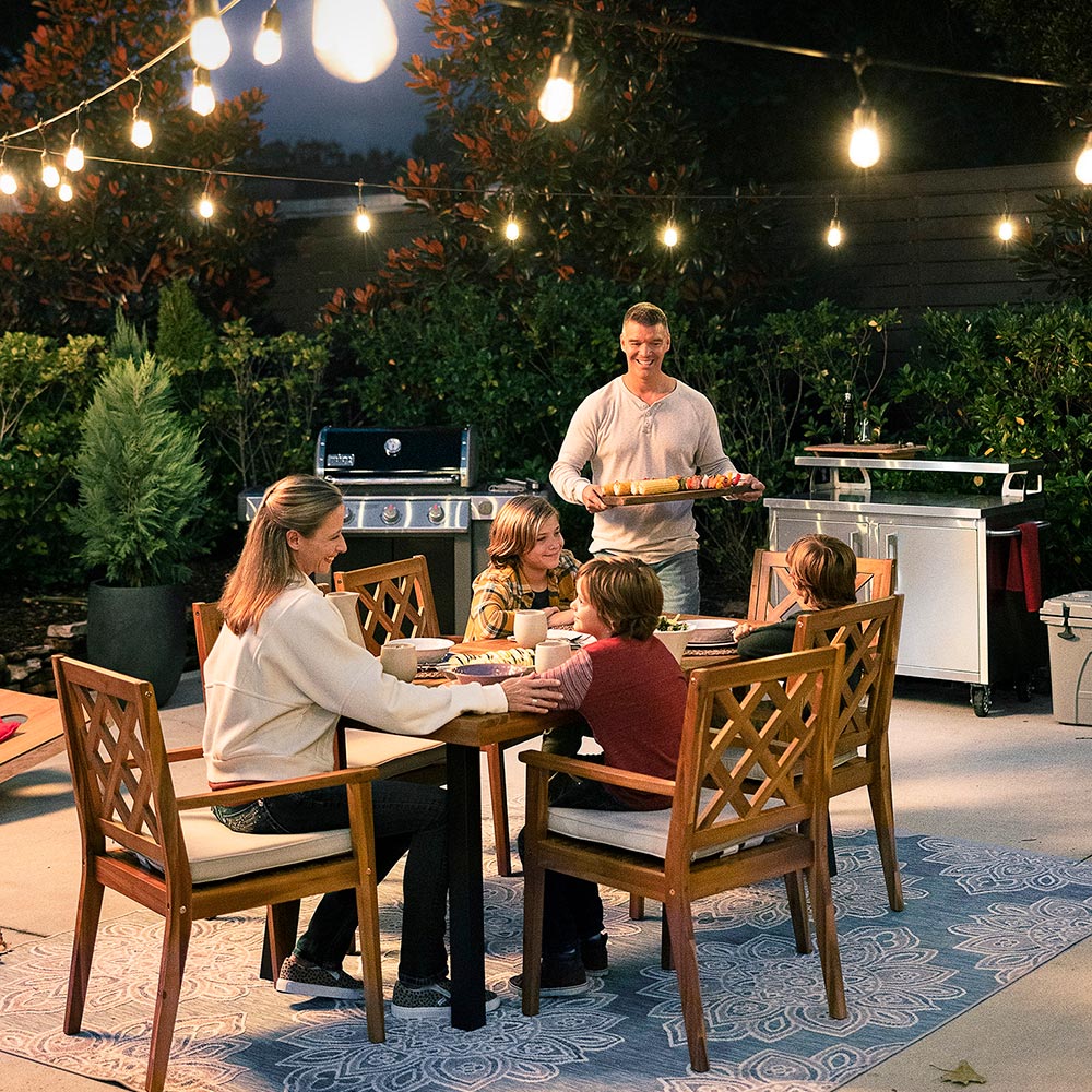 Family enjoying a grilled dinner on a gently lit patio at dusk