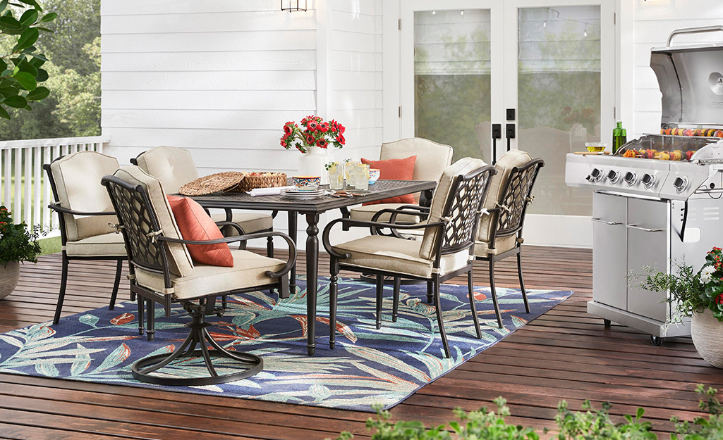 A patio dining table with chairs next to a barbecue grill.