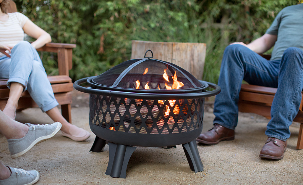 Three people sit on patio chairs next to a fire pit.