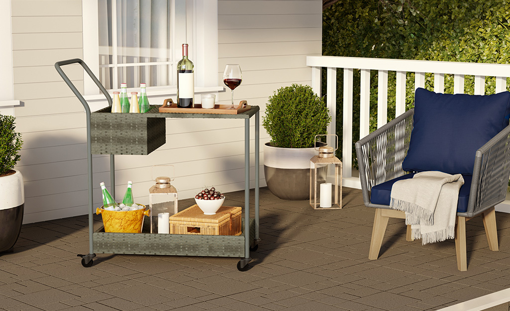 A mobile cart with a wine bottle and glass next to a patio chair.