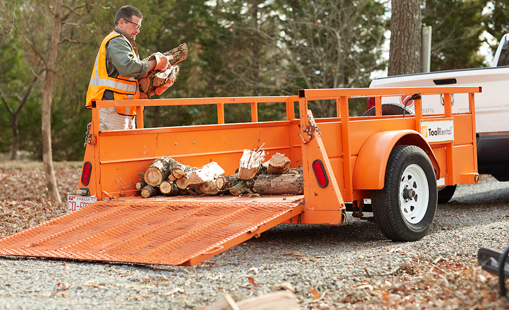 A man loading firewood on a utility trailer.