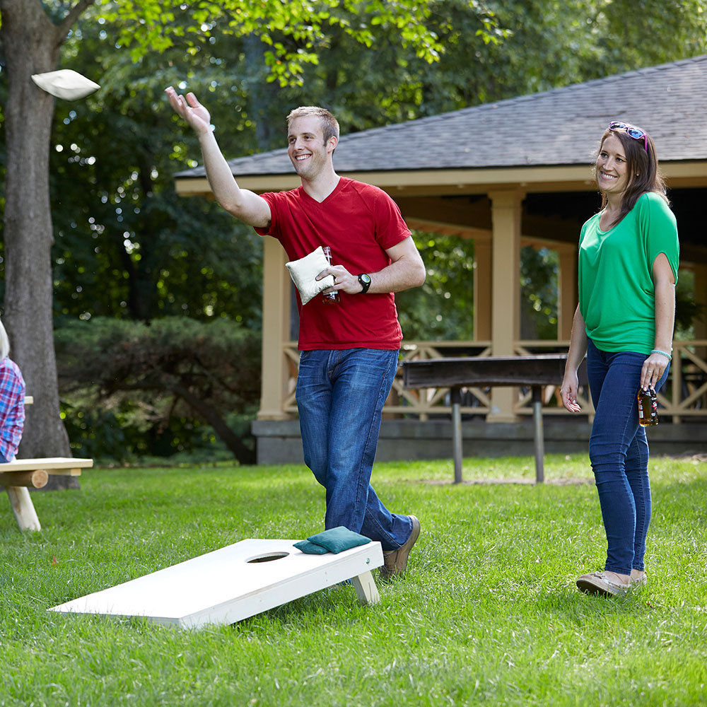 A couple plays a game of cornhole at a backyard tailgate. 