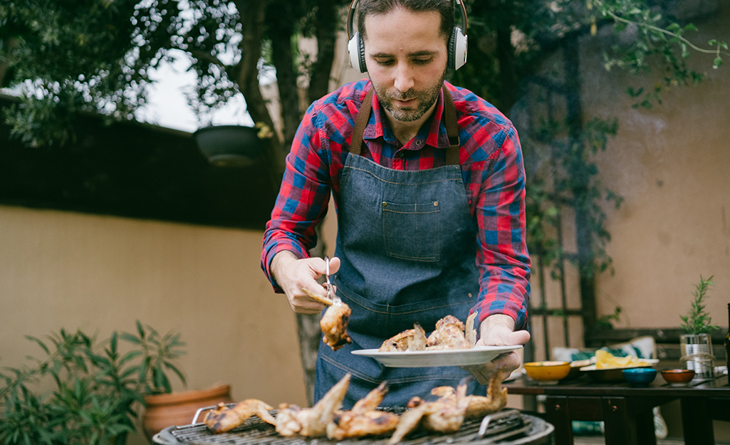 A man wears headphones to listen to a game while grilling tailgate food. 