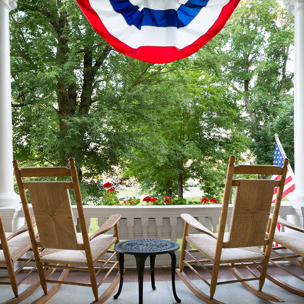 Rocking chairs sit under 4th of July bunting on a porch.