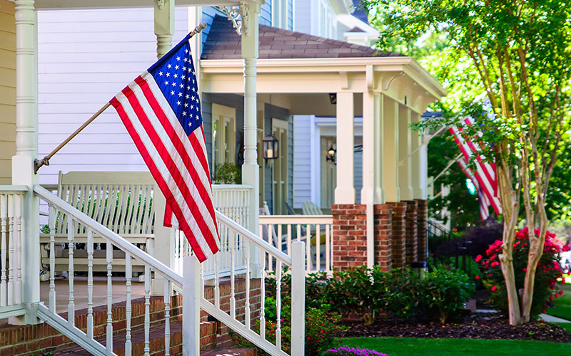 An American flag hangs from the post of a front porch.