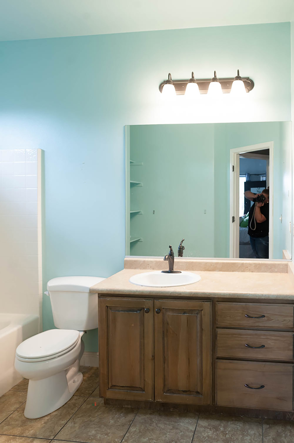 A bathroom with teal walls, brown floors, and an older wooden vanity.