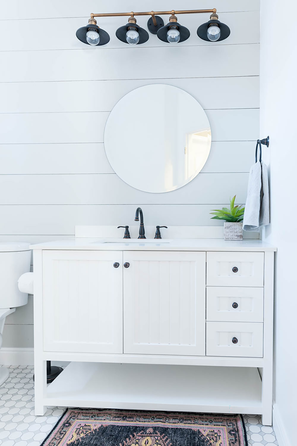 An updated bathroom with white shiplap walls, white tile floors and a white vanity.