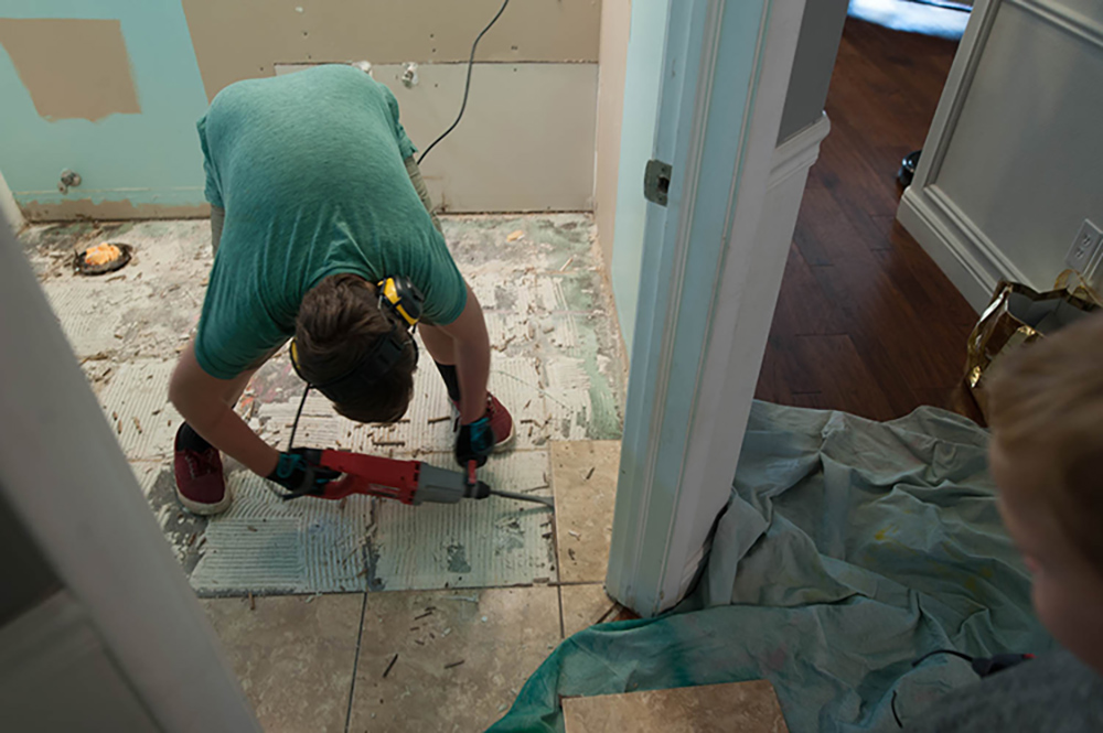 A person removing old tile from a bathroom floor.