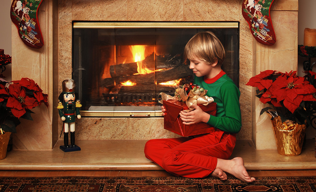 A child holds a gift while poinsettias flank the fireplace