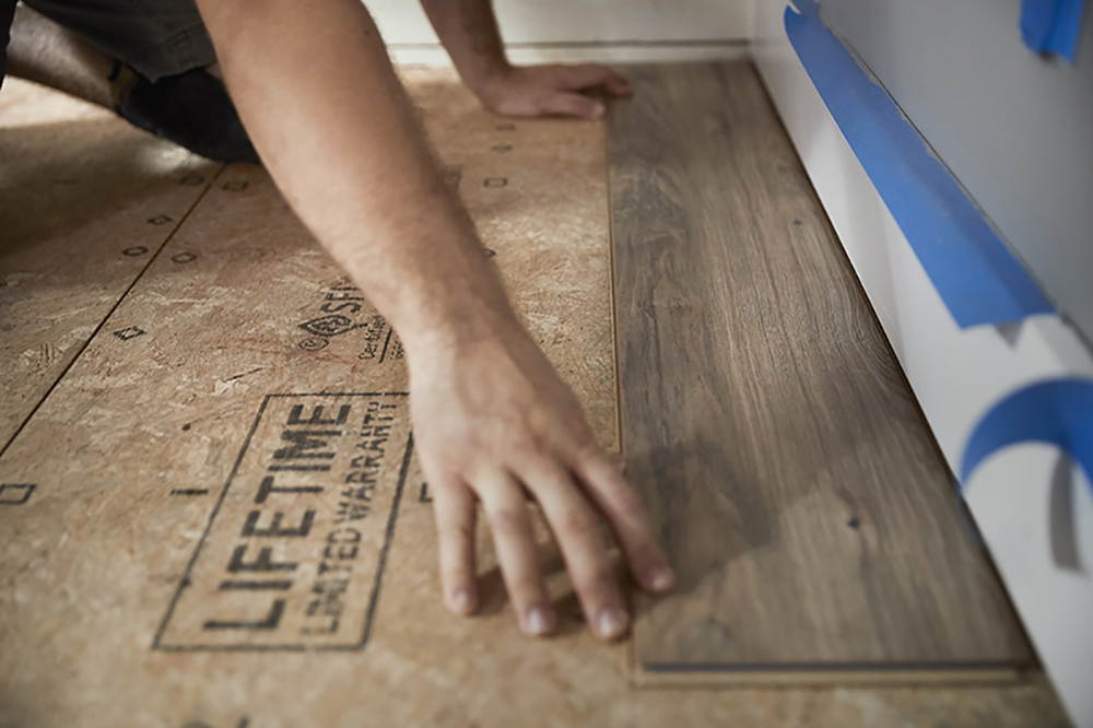A person installing the first laminate flooring plank.