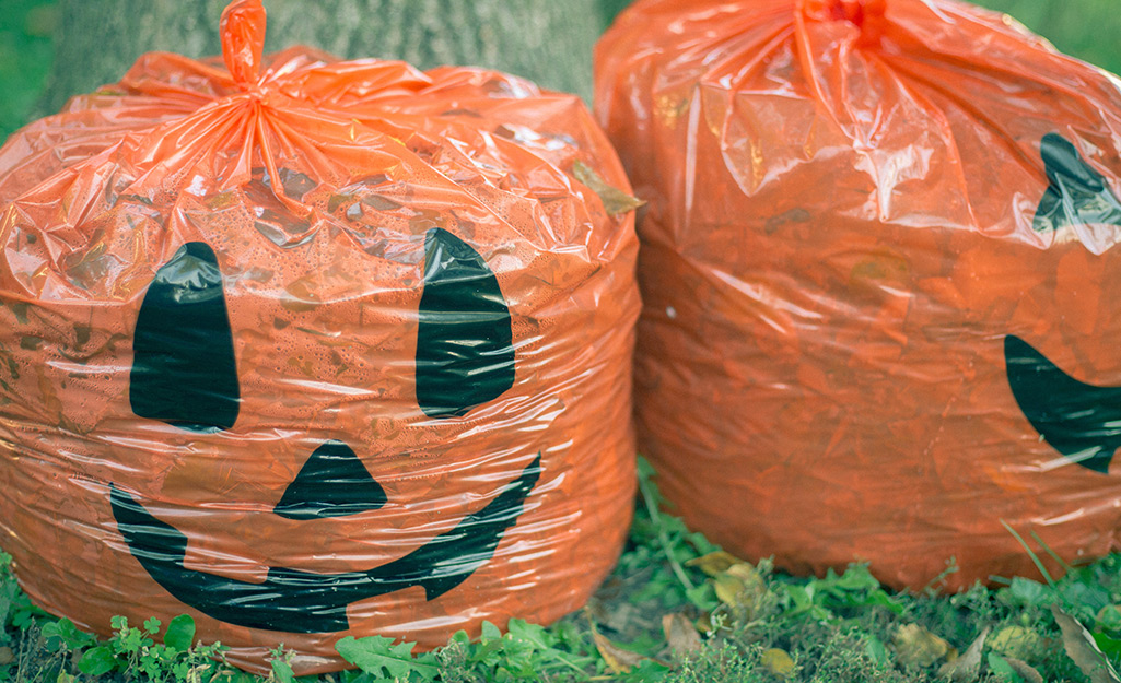 Festive pumpkin leaf bags sit on a lawn.