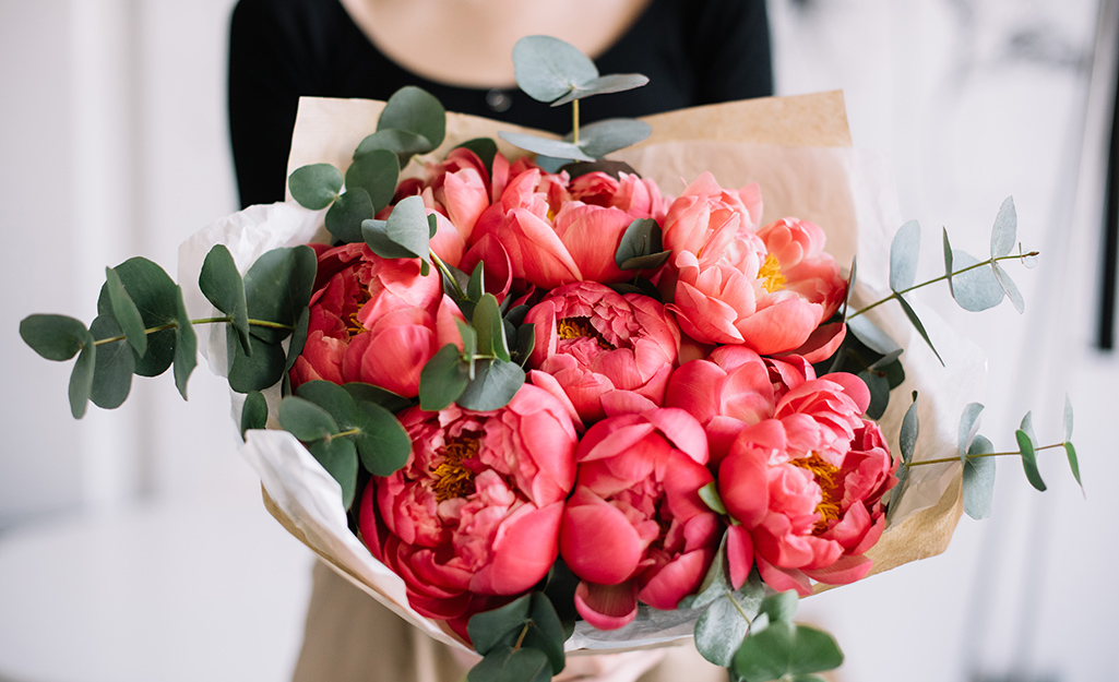 A woman holds a bouquet of red peonies wrapped in paper.