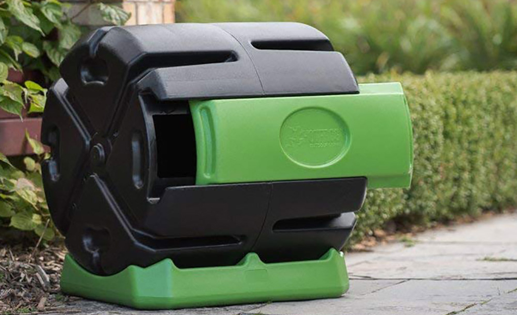 A plastic container that holds compost stands on a walkway in a yard.