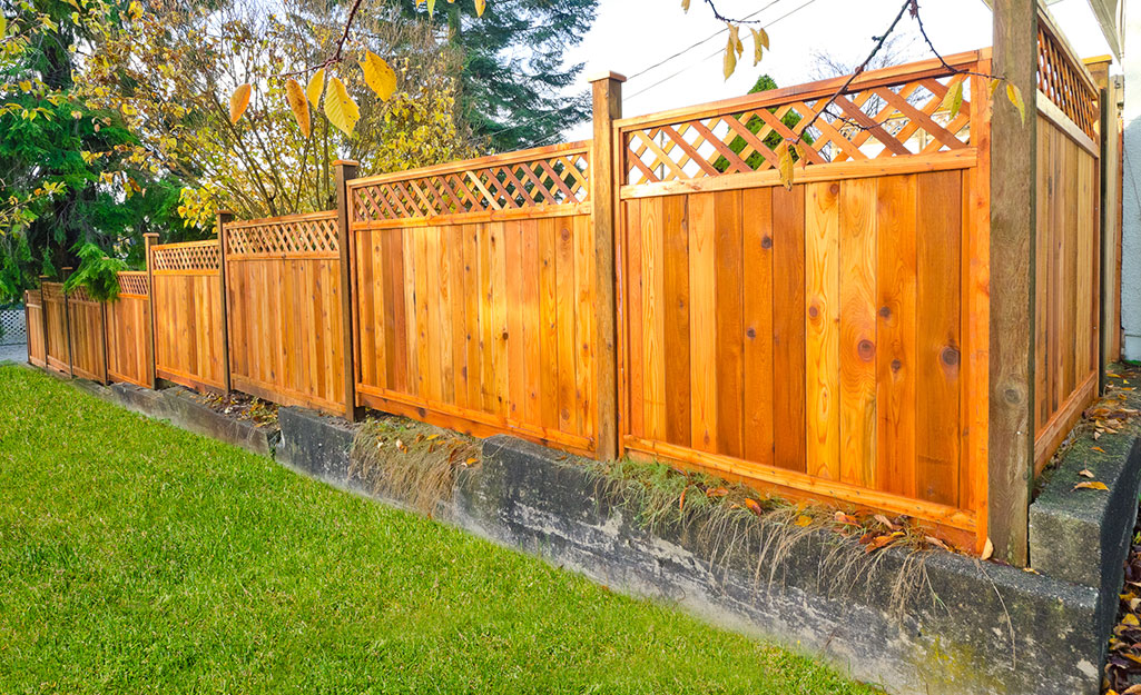 A wooden fence with a lattice accent on top stands along the edges of a yard.