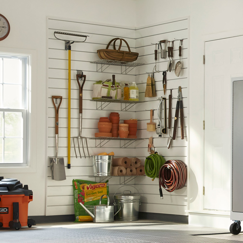 A corner of a garage holds a selection of garden tools hanging on the wall and sitting on shelves.