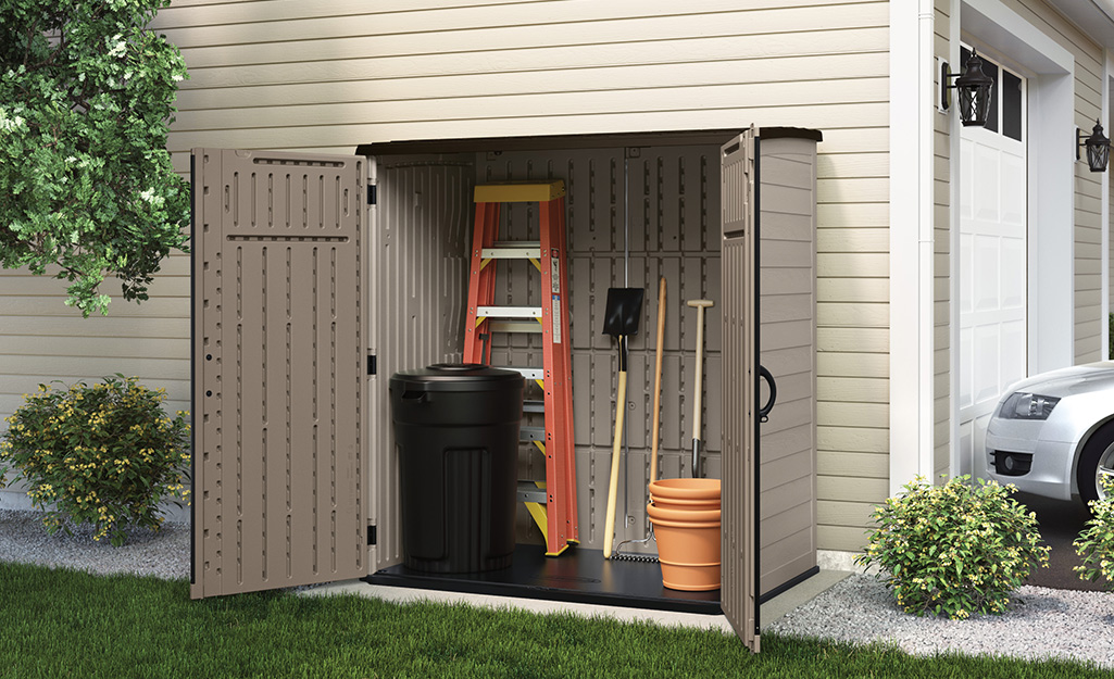 A small portable shed holds a ladder, tools and a trash can.