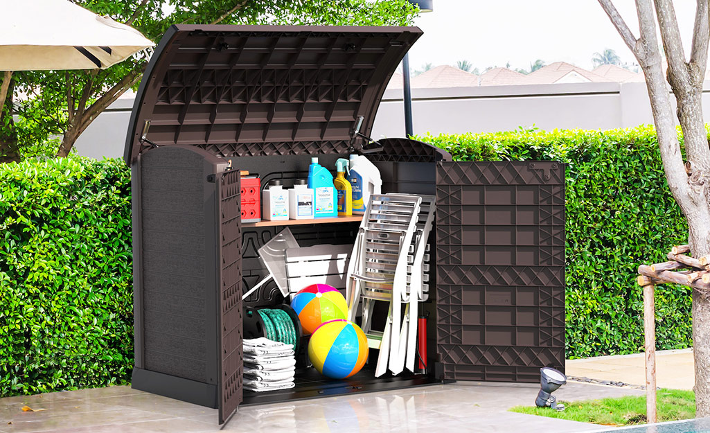 A deck box holds gardening supplies, patio chairs and beach balls.