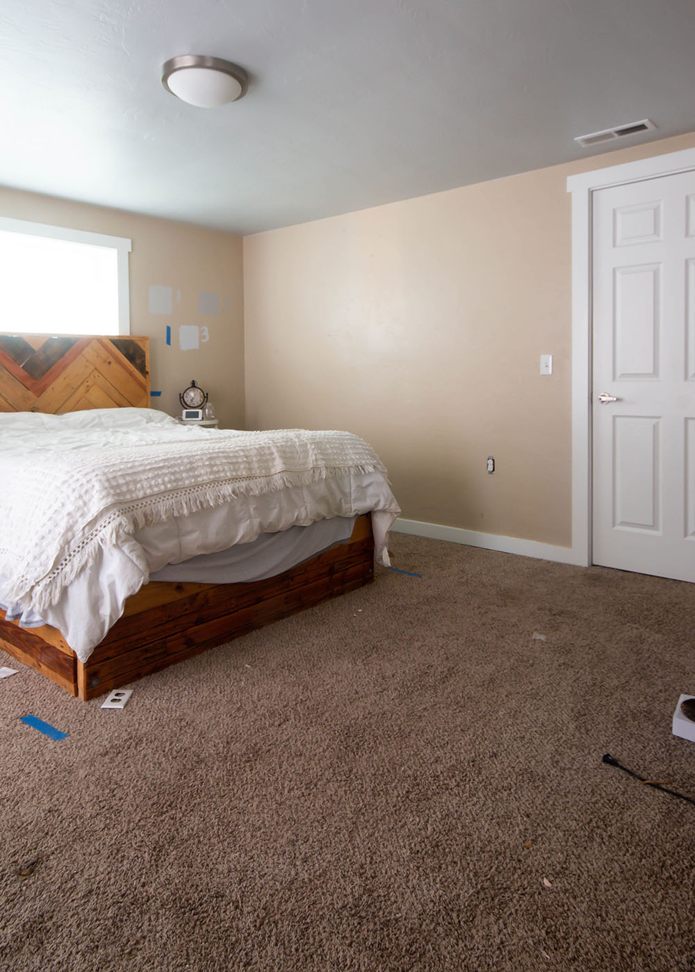 Bedroom with a bed, a white comforter, beige walls, beige carpet, one window, and one white closet door.