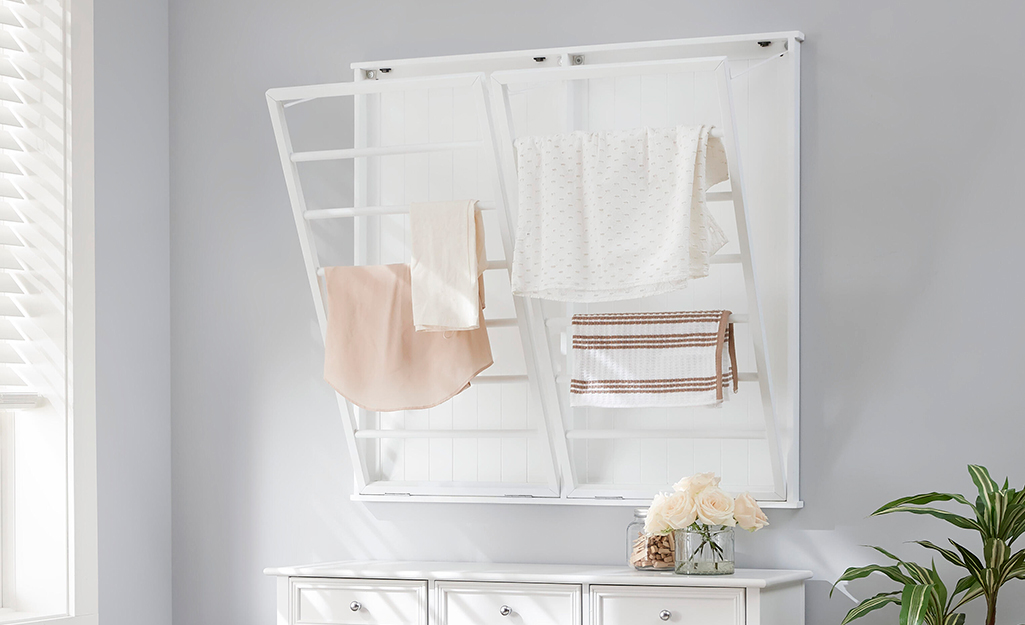 A collapsable laundry rack above a white storage cabinet.