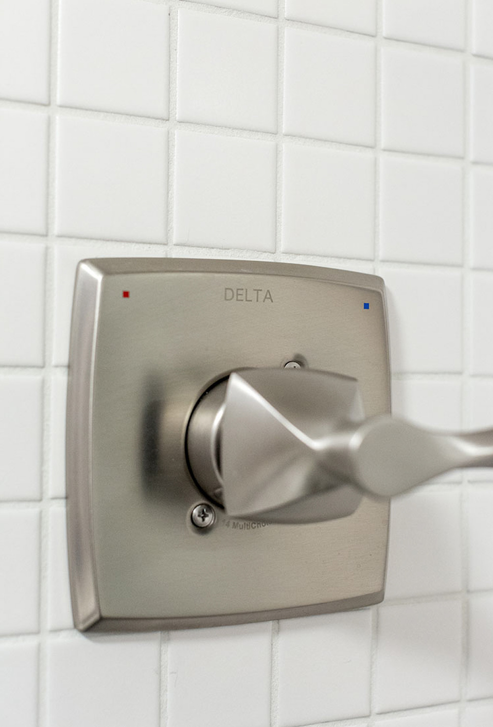 A silver shower faucet on a white tile wall.