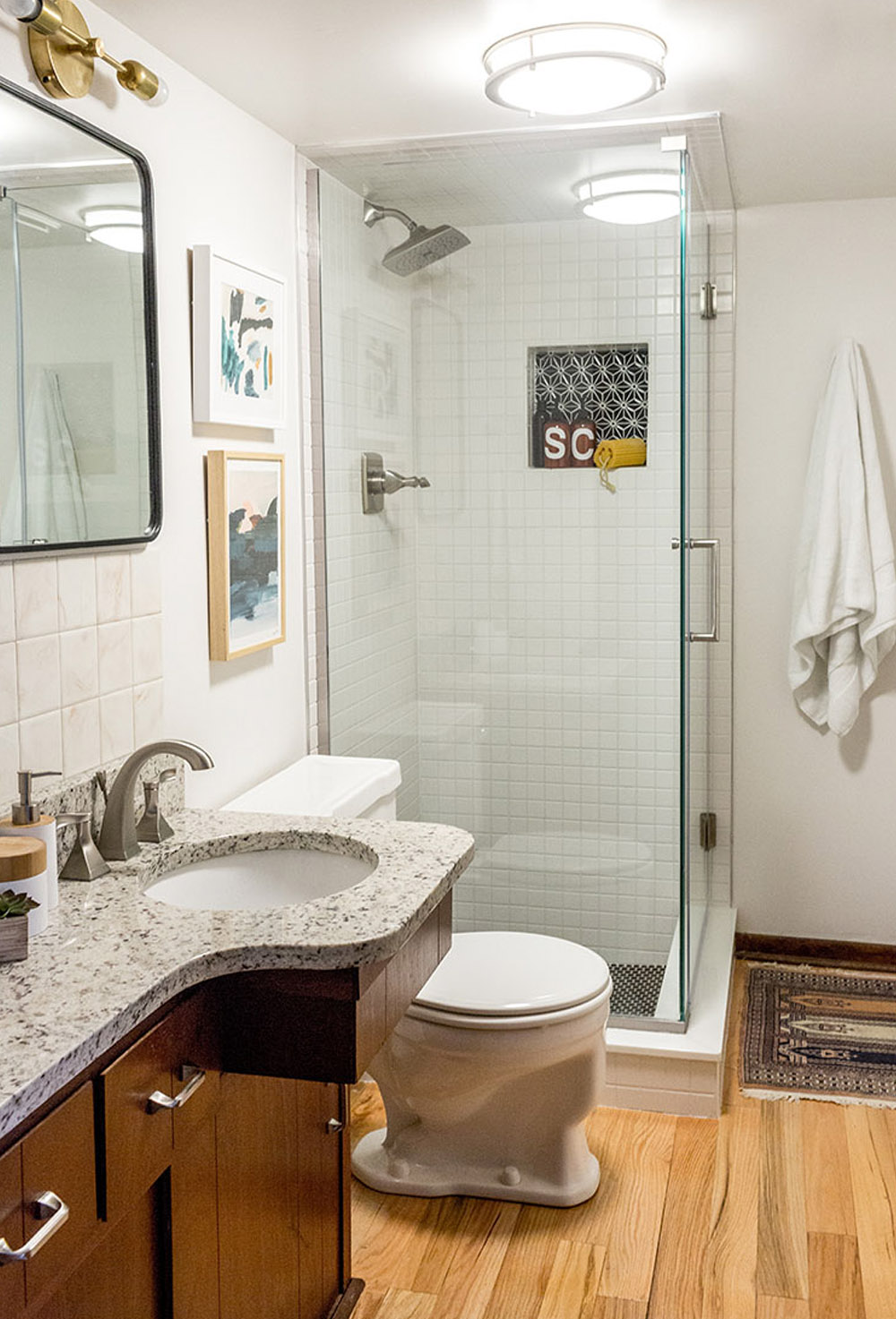 Marble bathroom countertop with a white hand towel, silver appliances and white soap dispenser, cream wall tile, a mirror and framed wall art.