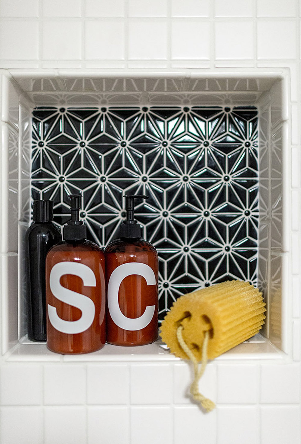 White tiled shower and a shelf with blue tile and shampoo dispensers.