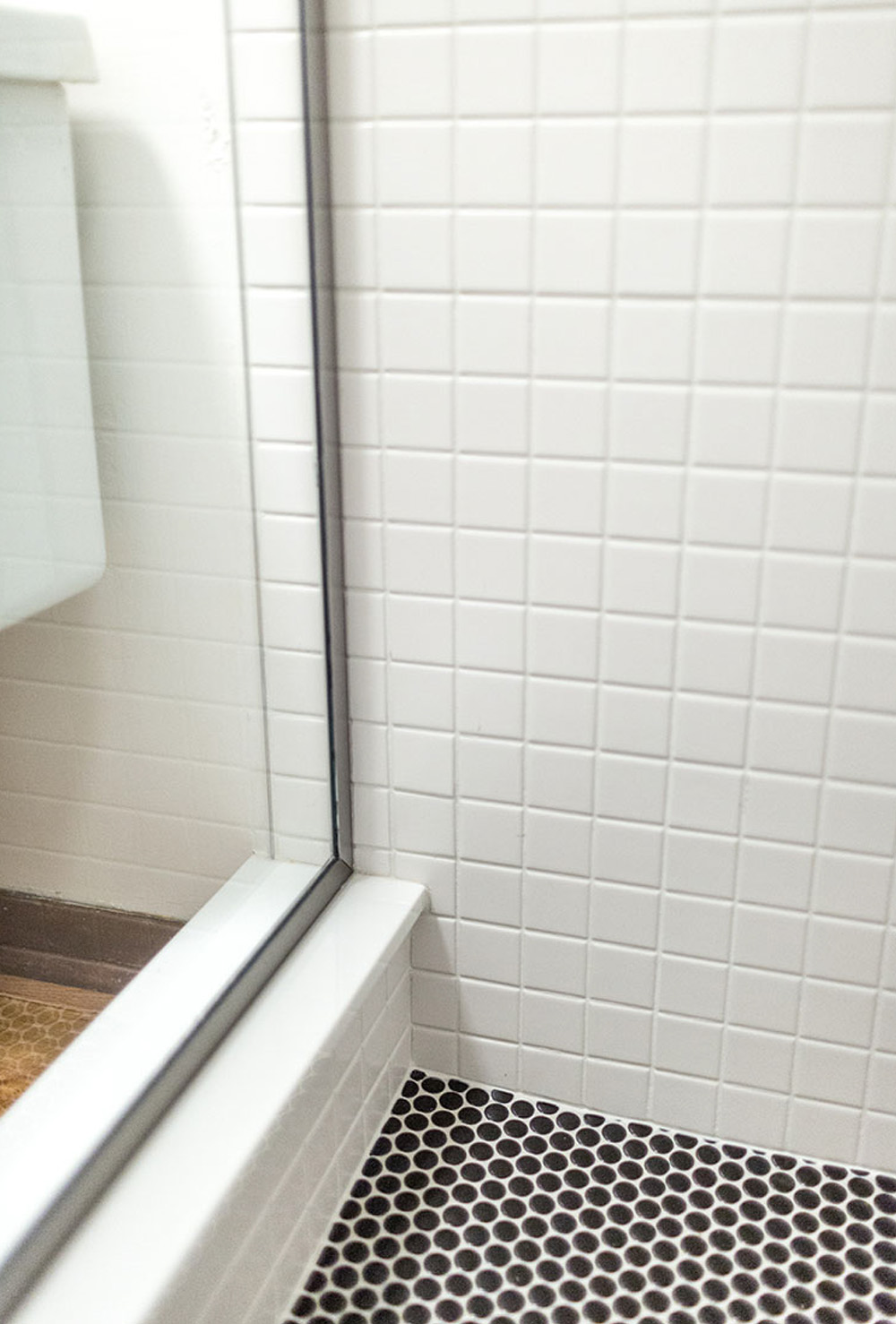 White tiled shower with a glass door and black tiled floor.