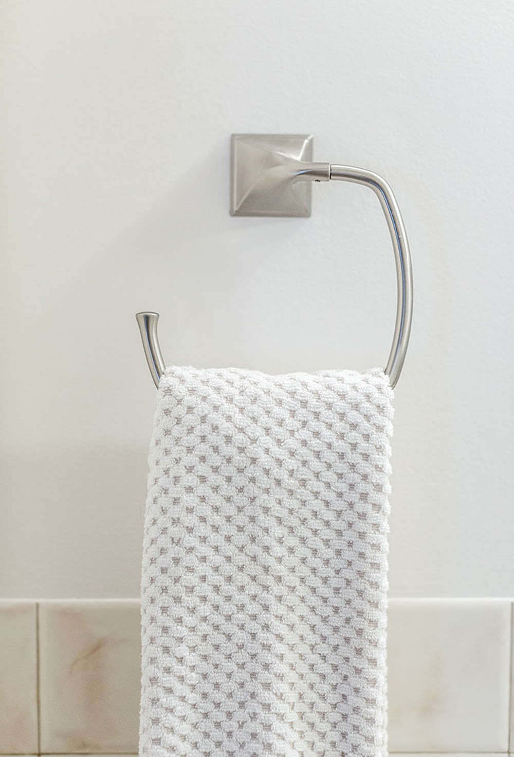 A silver hand towel holder with a white linen against a white and beige tiled wall.