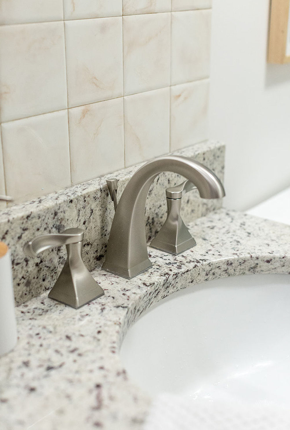 A marble countertop with silver sink faucet against a beige tiled wall.