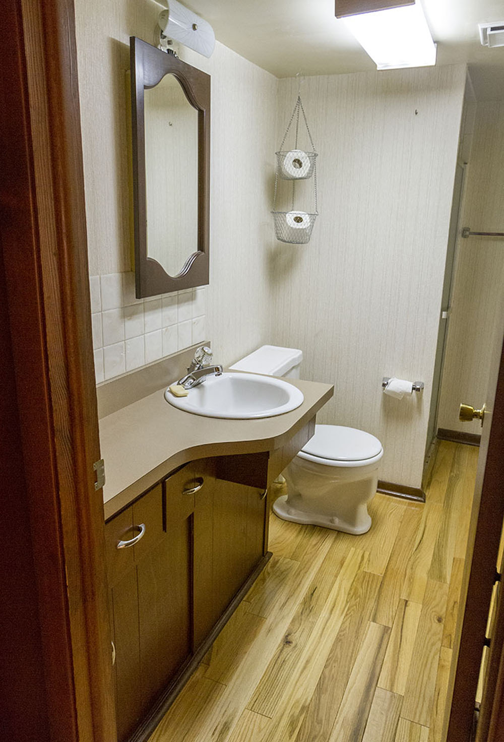 A bathroom with a brown vanity, white sink, white toilet, mirror and wood flooring.