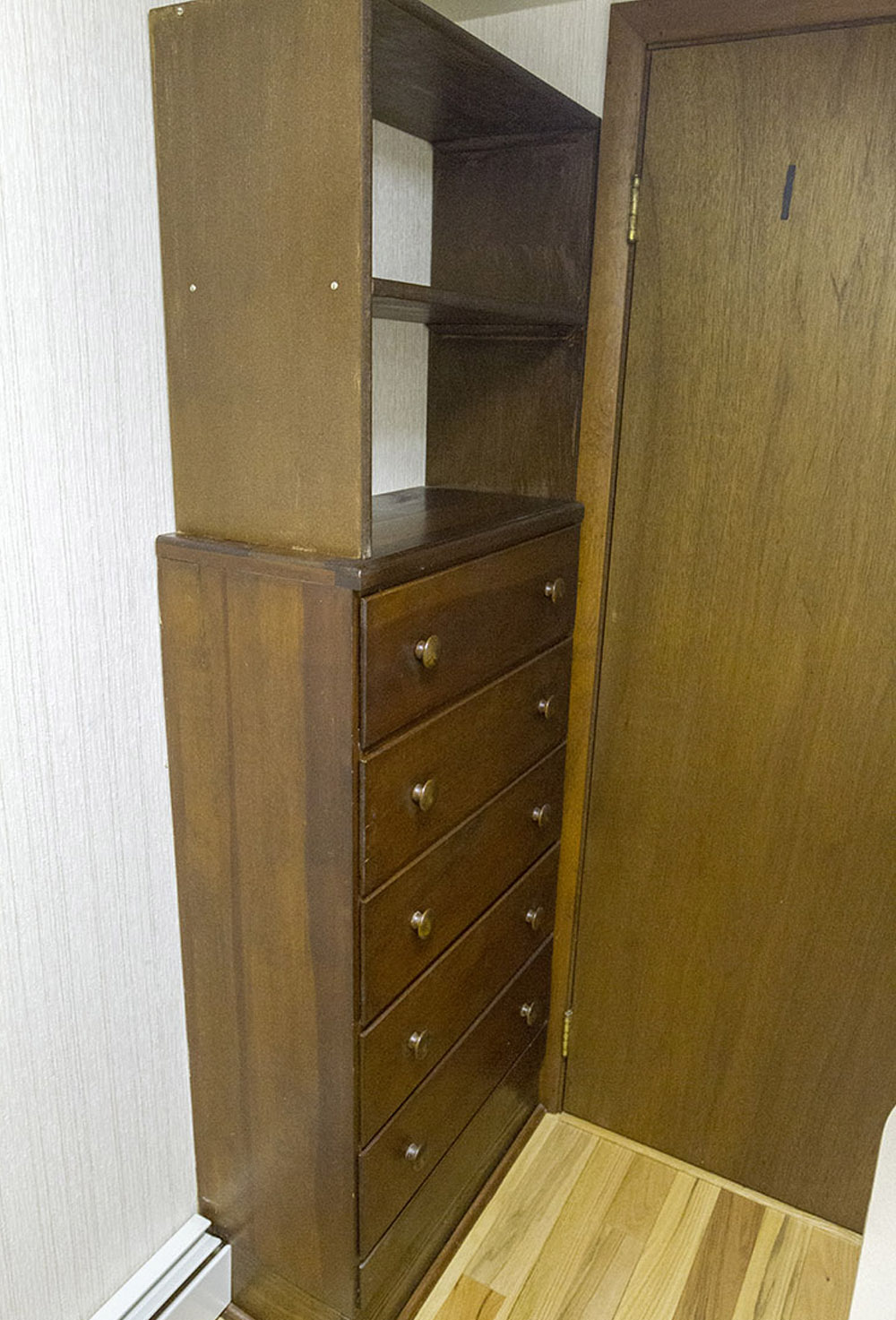 A wooden dresser with shelving on top against a white wall.
