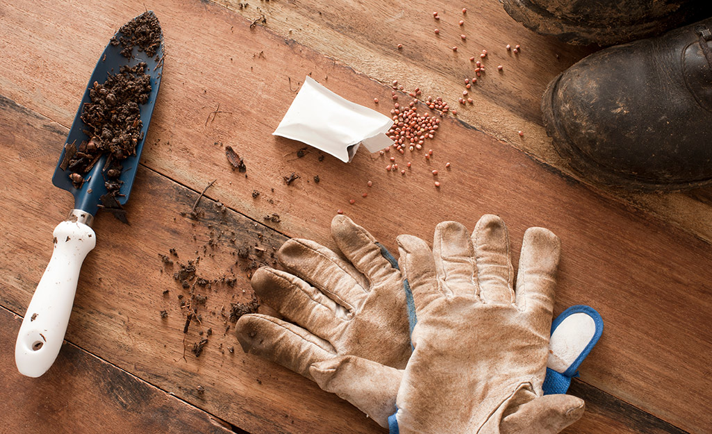 Garden trowel, garden gloves and seeds spread out on a wood table.