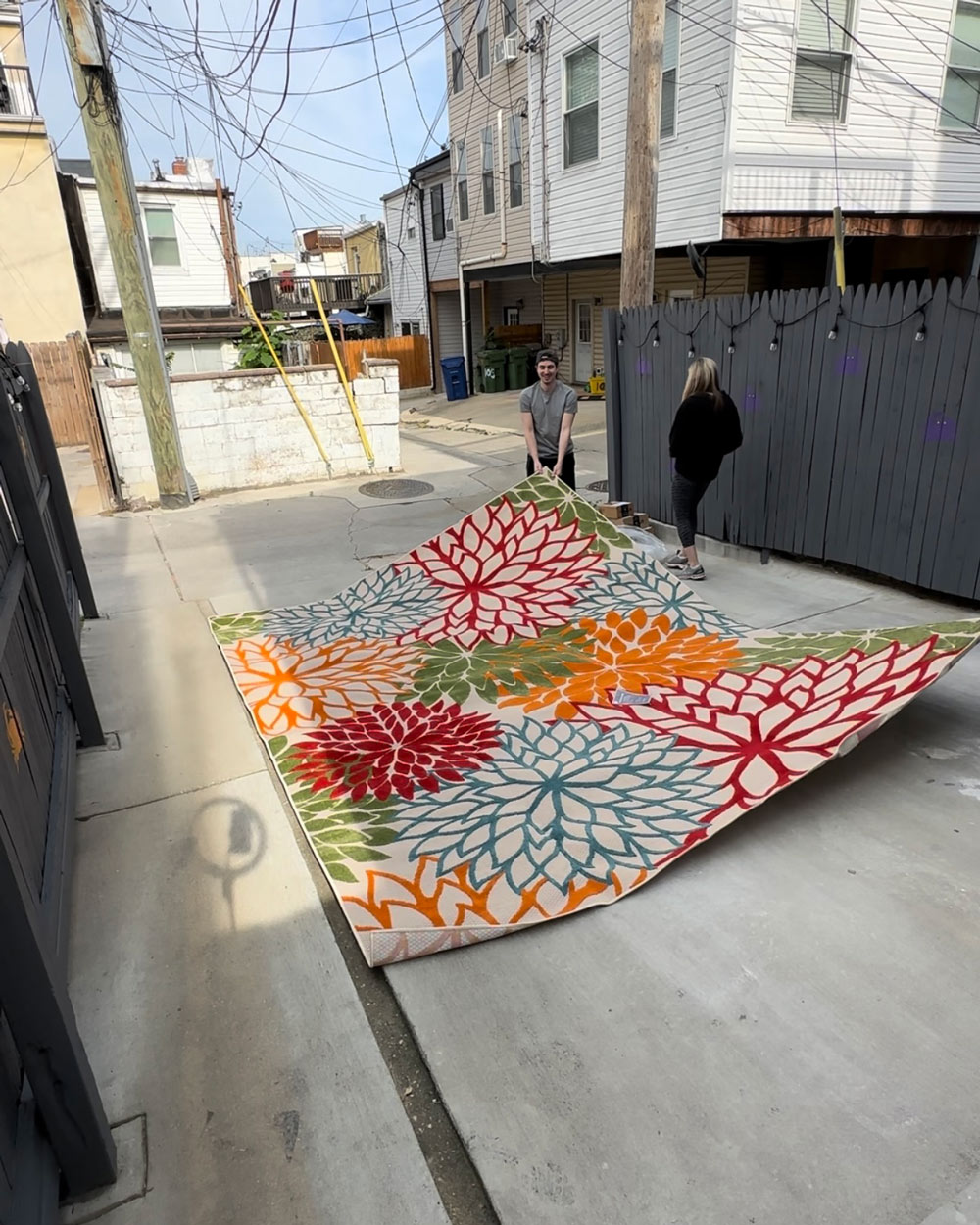 Two people moving a colorful outdoor rug with green, blue, red and orange flowers. Two people moving a colorful outdoor rug with green, blue, red and orange flowers.