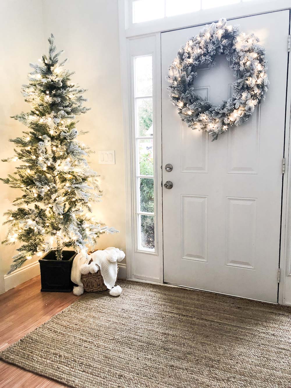 An oversized holiday wreath and Christmas tree decorated with lights hanging on back of door