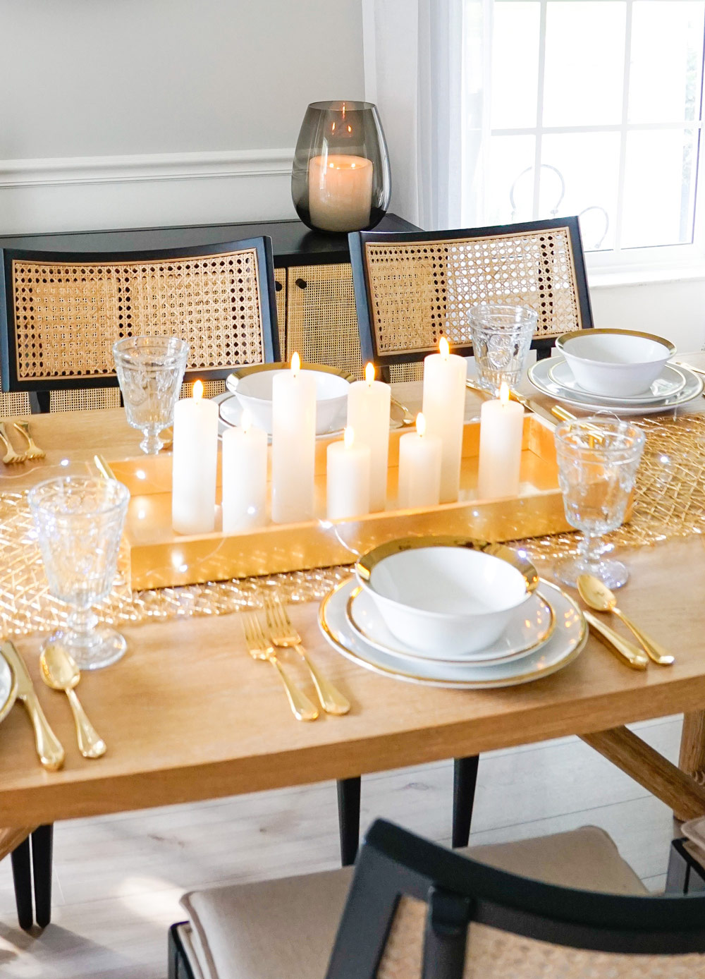 Table decorated with dinnerware, gold flatware, glasses, and a gold tray filled with candles.